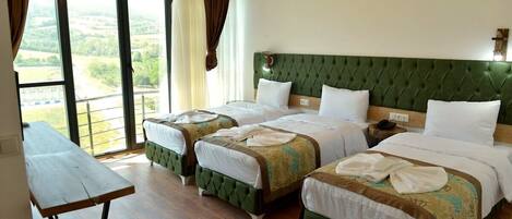 A hotel room with three beds, a wooden table, and a view of the countryside.
