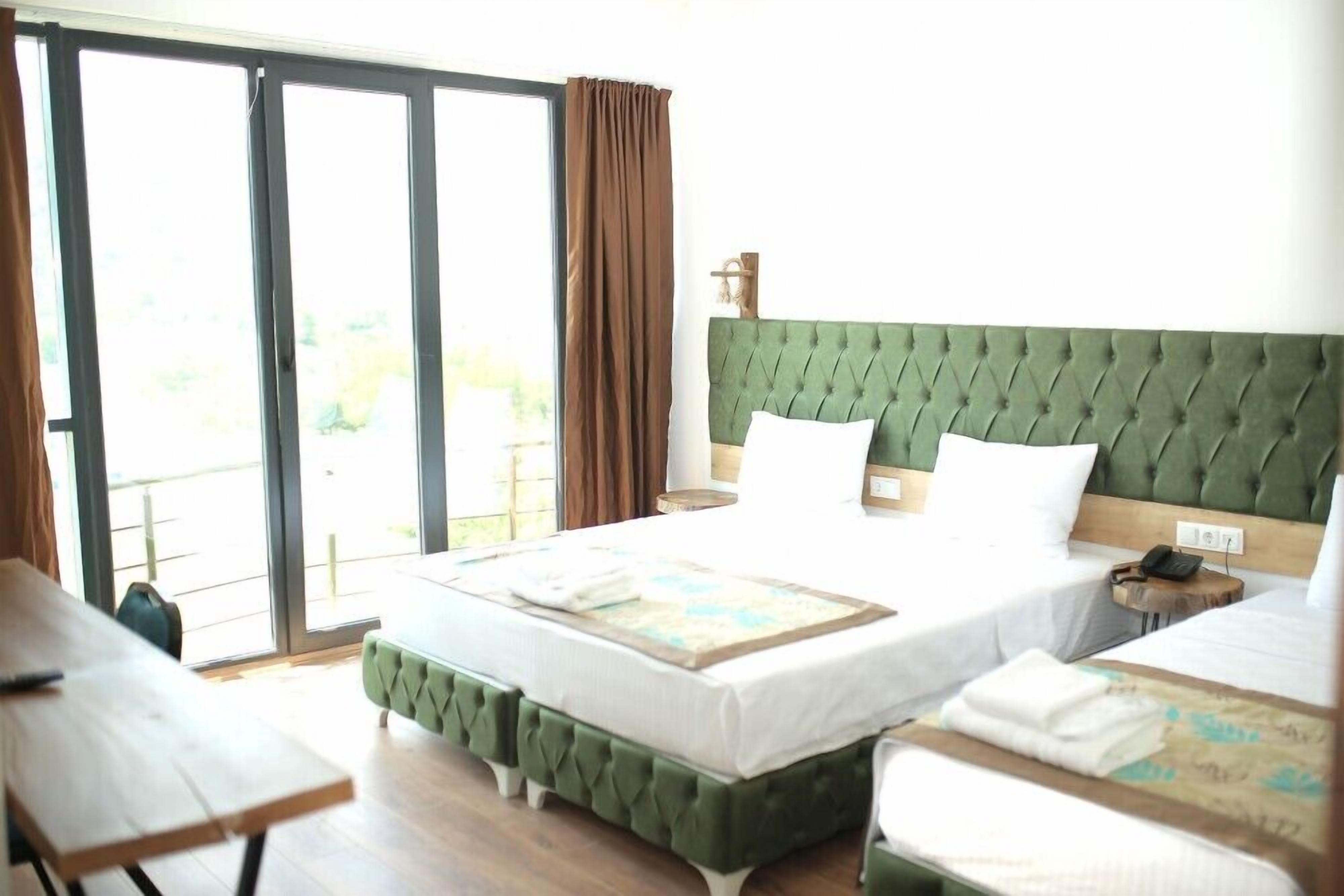 A hotel room with a large bed, a smaller bed, a desk, and a sliding glass door to the outside.