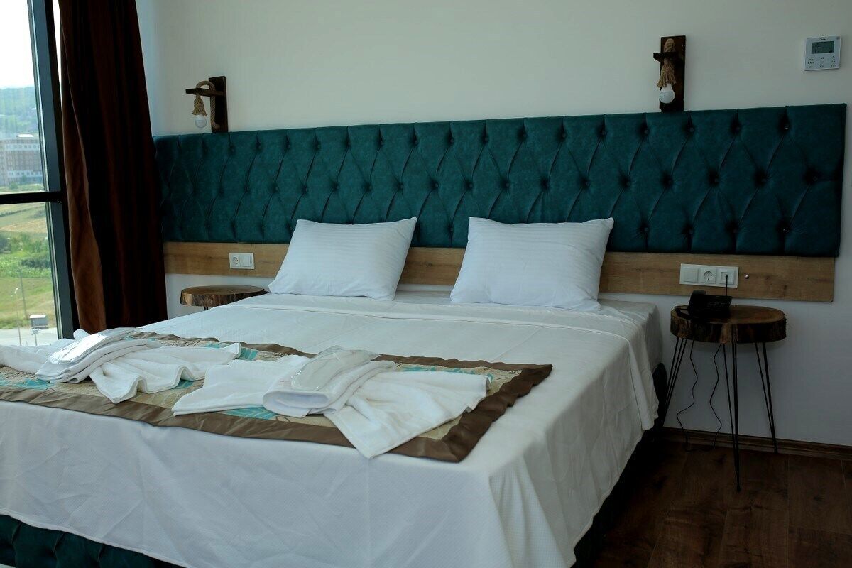 A neatly made bed with white linens and a teal upholstered headboard.