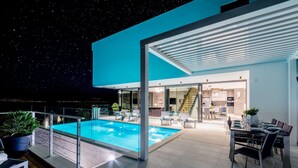 A modern outdoor pool area with a covered seating area, a dining setup, and a view of the interior. - Luxury Villa Complex Pax & Vitae With Heated Infinity Pools, 16 Sleeps (Sutivan)