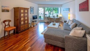 A living room with a sofa, a wooden cabinet, a TV, and a dining area with a table and chairs. - Residenz Barke App 10 (Scharbeutz)