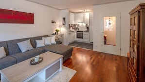 A modern living room with a grey sectional sofa, a white coffee table, and a kitchen in the background. - Residenz Barke App 10 (Scharbeutz)