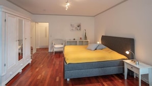 A bedroom with a bed, bedside table, wardrobe, and a chair. - Residenz Barke App 10 (Scharbeutz)