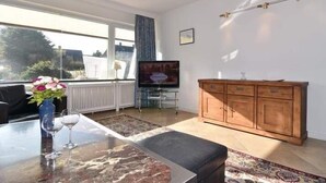 Ein Wohnzimmer mit Fernseher, Holzschrank und Glastisch mit Weingläsern.
