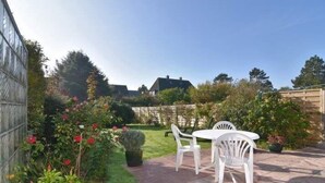 Eine Terrasse mit Tisch und Stühlen, umgeben von üppiger Bepflanzung und blühenden Pflanzen.