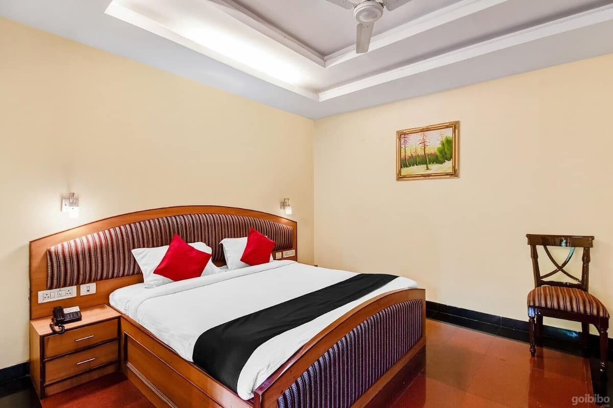 A hotel room with a large bed, a wooden headboard, a nightstand with a telephone, and a chair.