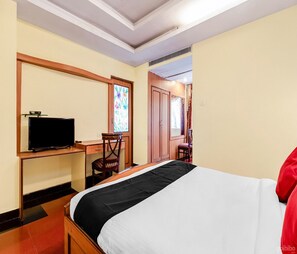 A hotel room with a bed, a desk with a television, a chair, and a door leading to another room.