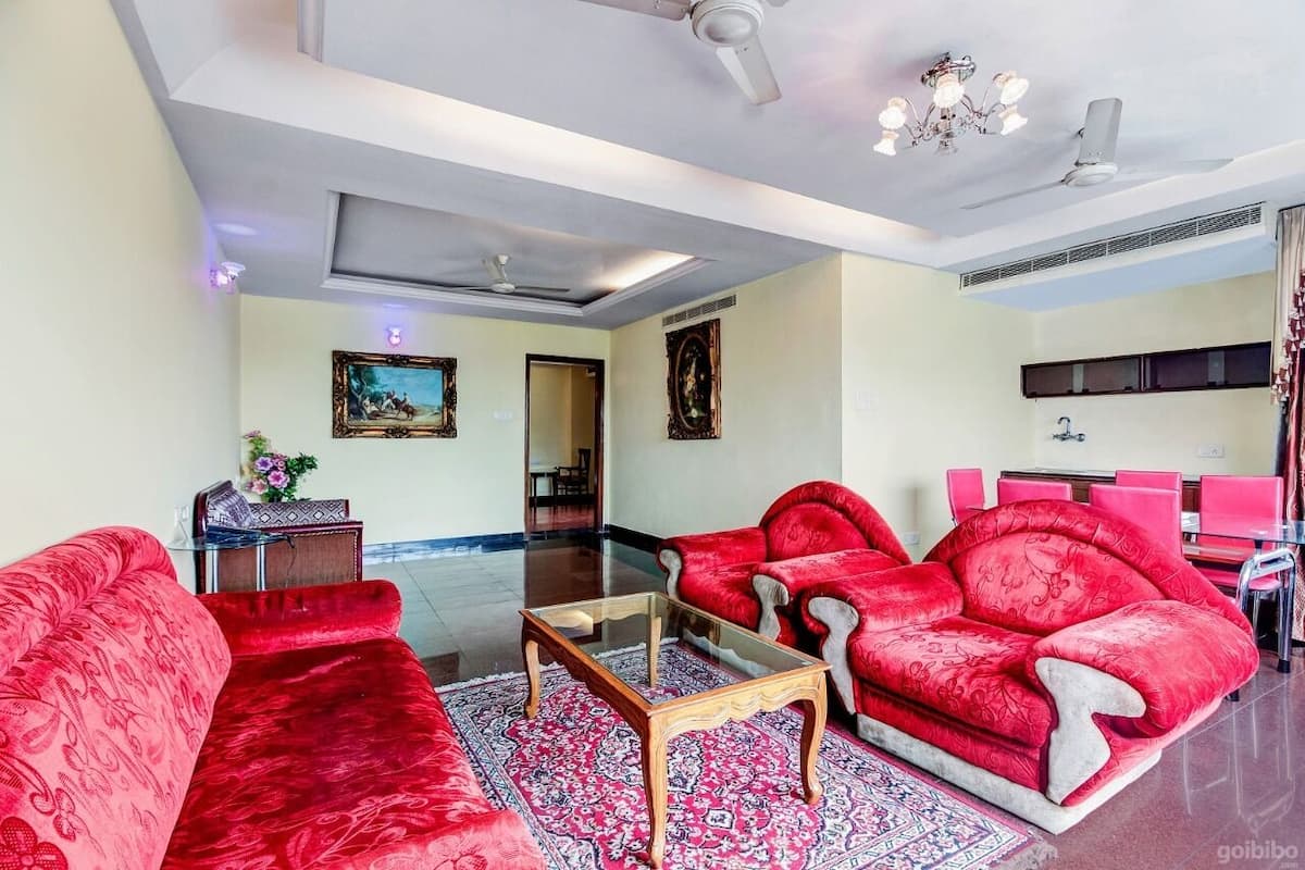A spacious living room with red sofas, a glass coffee table, and a chandelier.