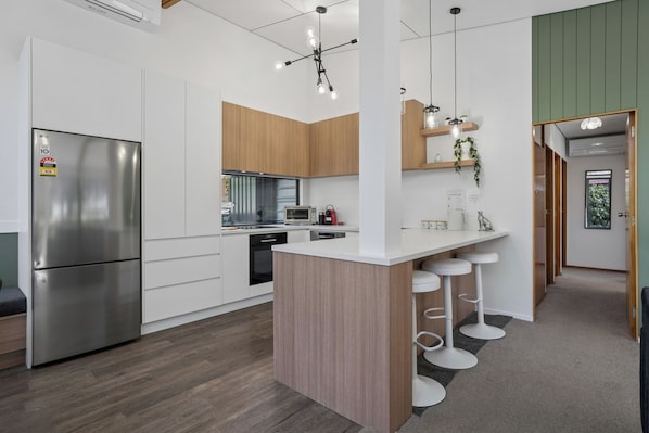 Una cucina moderna con frigorifero in acciaio inox, mobili in legno, un'isola centrale con sgabelli da bar e illuminazione a sospensione.