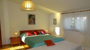 A bedroom with a bed, bedside lamps, a window with curtains, and a hanging light fixture. - Apartment Vlahov (Barilovic)