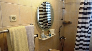 A bathroom with a shower, a towel rack with towels, a mirror, a soap dispenser, and a shower caddy. - Villa Lena Ap.1 (Podgora)