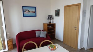Una sala de estar con un sofá rojo, una mesita de madera, una mesa blanca con frutero y una puerta.