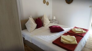 Una cama bien hecha con ropa de cama blanca y roja, una mesita de noche con lámpara y una pared decorada con dos platos ornamentales.
