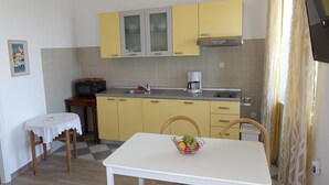 Una cocina compacta con armarios amarillos, una encimera blanca y una pequeña mesa de comedor con una cesta de fruta.