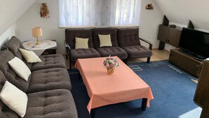 A cozy living room with a sofa set, a coffee table with flowers, a TV, and a window with sheer curtains. - Ferienhaus Hirschrudel - Ferienwohnung 3 (Katzow)
