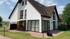A two-story house with a sloped roof, large windows, and a covered patio area. - Ferienhaus Hirschrudel - Ferienwohnung 3 (Katzow)