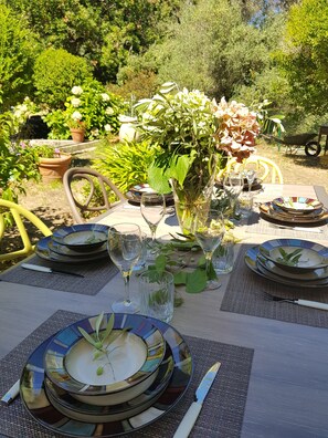 An outdoor dining table set with plates, glasses, and cutlery, surrounded by potted plants and a wheelbarrow. - Independent villa with private garden in Cap Corse, between sea and forest (CAGNANO)