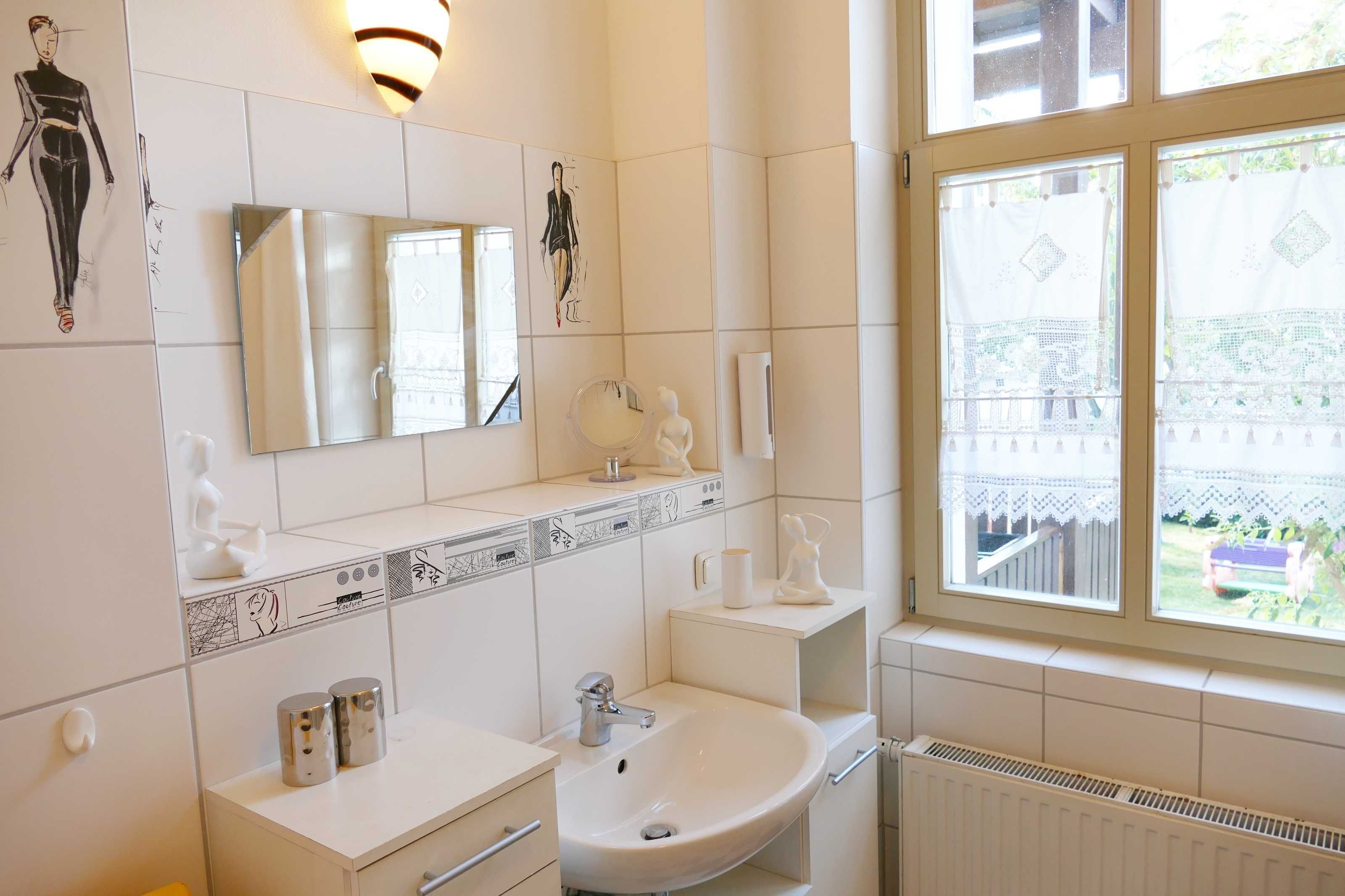 Ein modernes Badezimmer mit einem großen Spiegel, weißen Fliesen, einem Waschbecken und einem Fenster mit Blick ins Freie.