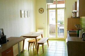 Una cocina con una mesa de comedor, sillas, un reloj y vistas por la puerta.