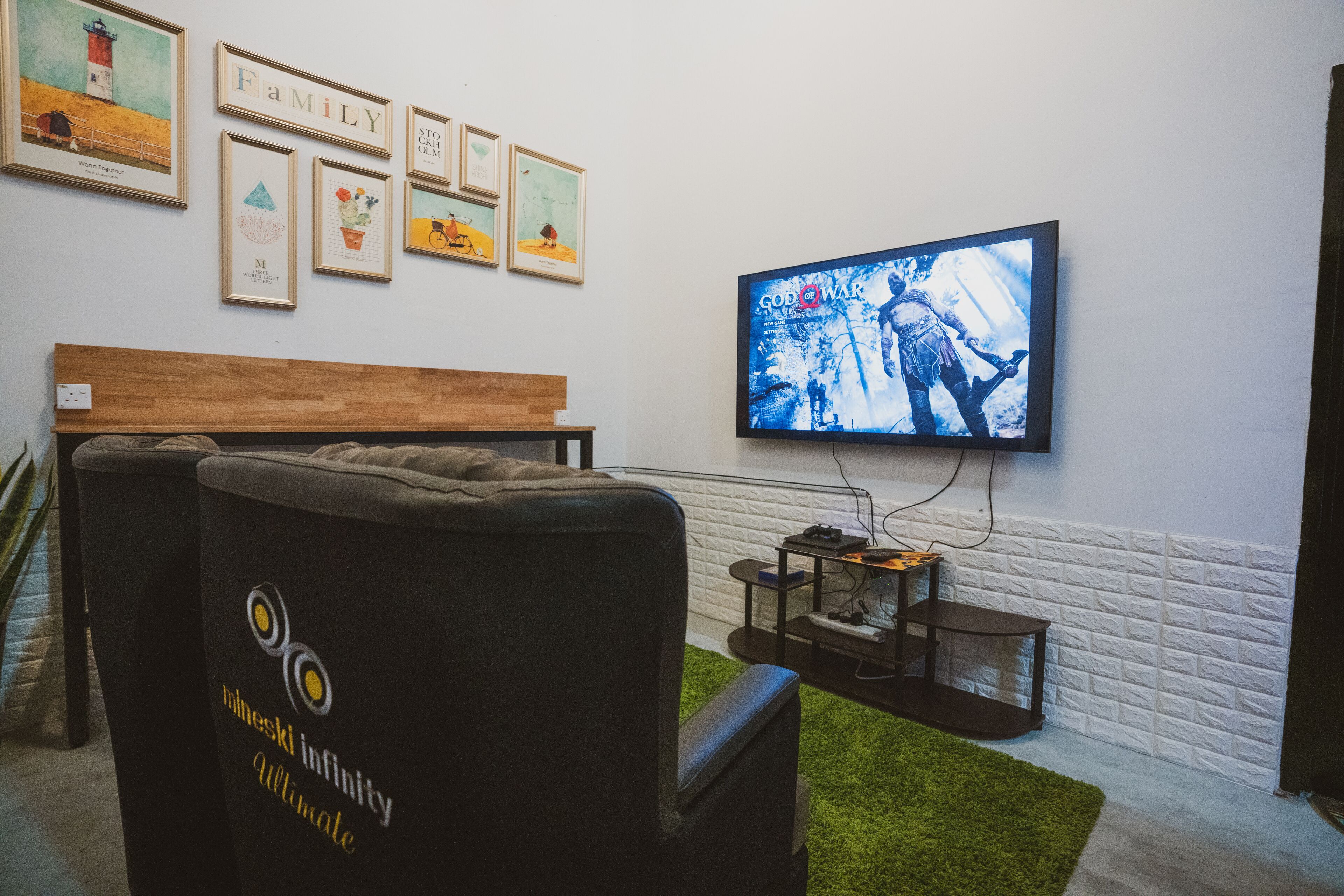 A room with a television mounted on the wall displaying a movie, a couch, a wooden bench, and framed artwork on the wall.