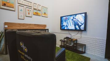 A room with a television mounted on the wall displaying a movie, a couch, a wooden bench, and framed artwork on the wall.
