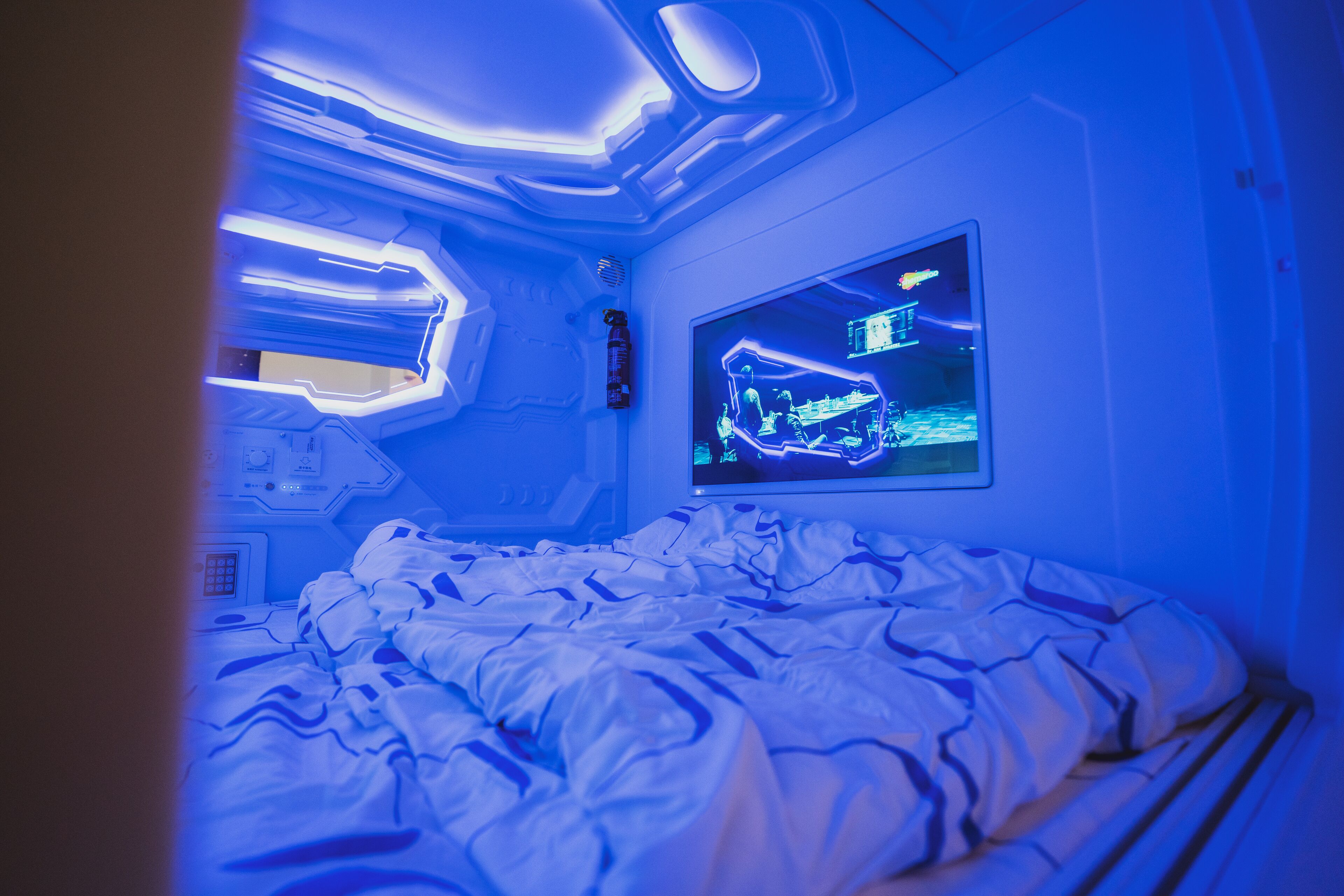 A room with a bed, a wall-mounted TV, and a control panel.
