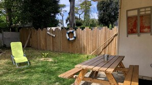 Una mesa de picnic de madera con bancos, una silla de jardín amarilla y una valla de madera con un flotador.