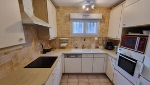 A compact kitchen with white cabinets, a black stove, a microwave, and a window above the sink. - Quiet T3 Apartment with Terrace and Equipped Kitchen, 300m from the Beach in Collioure (Collioure)