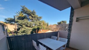 A balcony with a table and chairs, a stone wall, and a view of trees and buildings. - Quiet T3 Apartment with Terrace and Equipped Kitchen, 300m from the Beach in Collioure (Collioure)