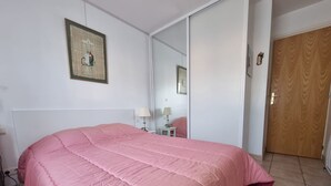 A bedroom with a large pink bed, a wooden door, and a mirror on the wall. - Quiet T3 Apartment with Terrace and Equipped Kitchen, 300m from the Beach in Collioure (Collioure)
