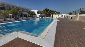 Une piscine équipée d’un escalier en métal, entourée de palmiers et bordée d’une terrasse carrelée.