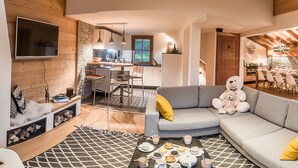 Una sala de estar moderna con un sofá gris, un televisor montado en la pared y un comedor con muebles de madera.