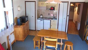 Une cuisine compacte comprenant une table et des chaises, un four à micro-ondes, un petit réfrigérateur et une bouilloire.