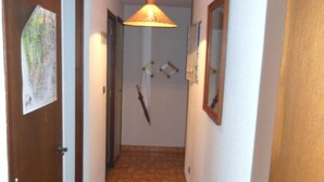 Un couloir étroit au sol carrelé, avec une lampe suspendue, une porte ornée d’une carte et un miroir accroché au mur.