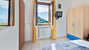 Une chambre à coucher avec un lit, une fenêtre avec des rideaux, un radiateur, une télévision et une armoire.