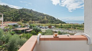 Un balcon donnant sur un paysage vallonné, une route et des voitures garées.