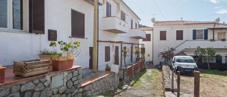 A narrow stone pathway leading to a white building with wooden shutters and potted plants.