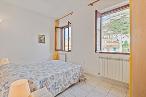 Une chambre à coucher avec un lit, une fenêtre donnant sur un beau paysage, un radiateur et un tableau accroché au mur.