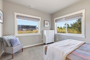 A bedroom with a bed, a dresser, a chair, and two windows with views of the outdoors. - Beach Dreamer-Updated, beautiful beach views (Pacific City)