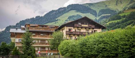 A hotel with multiple balconies, a wooden facade, and a view of green hills in the background.