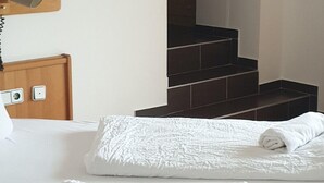 A hotel room with a bed, a wooden headboard, a white textured blanket, and a set of dark stairs leading to an upper level. - Hotel Sonnhof (Rauris)