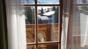 A room with a large window offering a view of snow-covered mountains and a town below. - Hotel Sonnhof (Rauris)