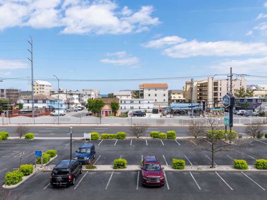 A parking lot with several cars, a white fence, and buildings in the background.