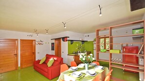 A compact living space with a dining area, a red sofa, and a kitchen area with a green backsplash. - Design cottage Treviso - the house in the park (Treviso)