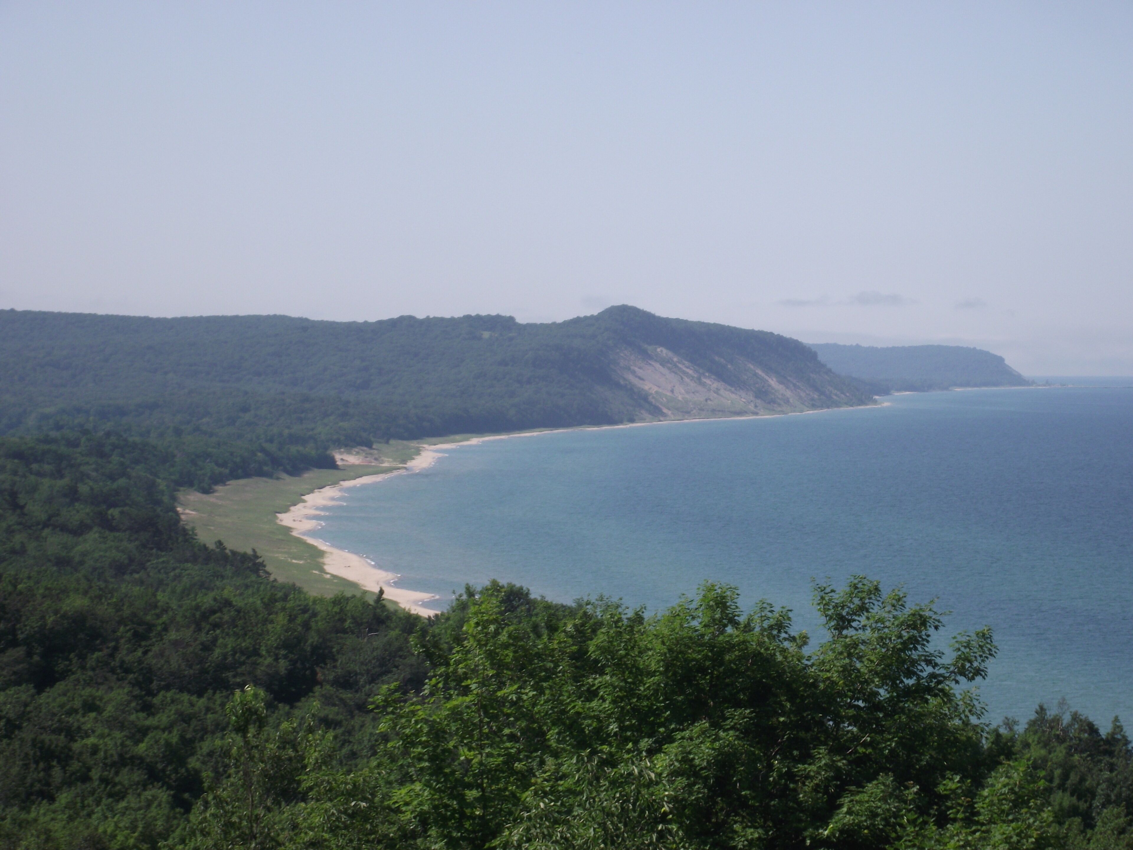 Eine Küstenlandschaft mit Strand, bewaldeten Hügeln und freiem Blick auf den Ozean.