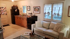 Un salon chaleureux avec un canapé blanc, une table basse en verre et un coin cuisine doté de meubles en bois, d’une cuisinière et d’un réfrigérateur.