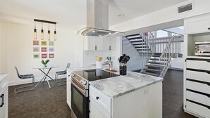Eine moderne Küche mit einer zentralen Kochinsel, Edelstahlgeräten und einer Treppe, die in einen oberen Bereich führt.