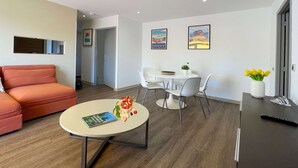 A modern living room with a sofa, a dining table with chairs, a small coffee table with a book and snacks, and a TV mounted on the wall. - Presqu'île du Capelan | Parking |Climatized |Preserved seaside |Calm assured (Bandol)