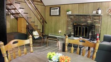 A living room with a fireplace, wooden walls, a staircase, and a dining table with flowers.