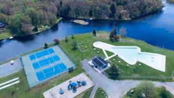 An aerial view of a lakeside property with a tennis court, a swimming pool, and a small building.
